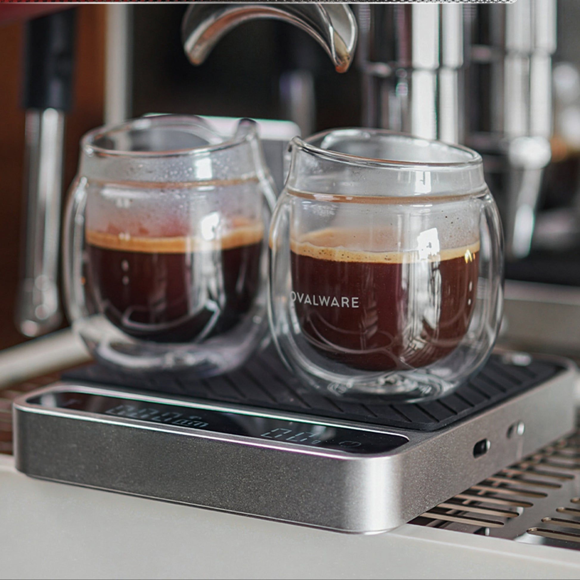 Two glass cups of coffee in front of an espresso machine with text about design and precision.